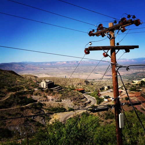 A telephone poll sits on a back drop of blue sky, red ridges and an old factory.